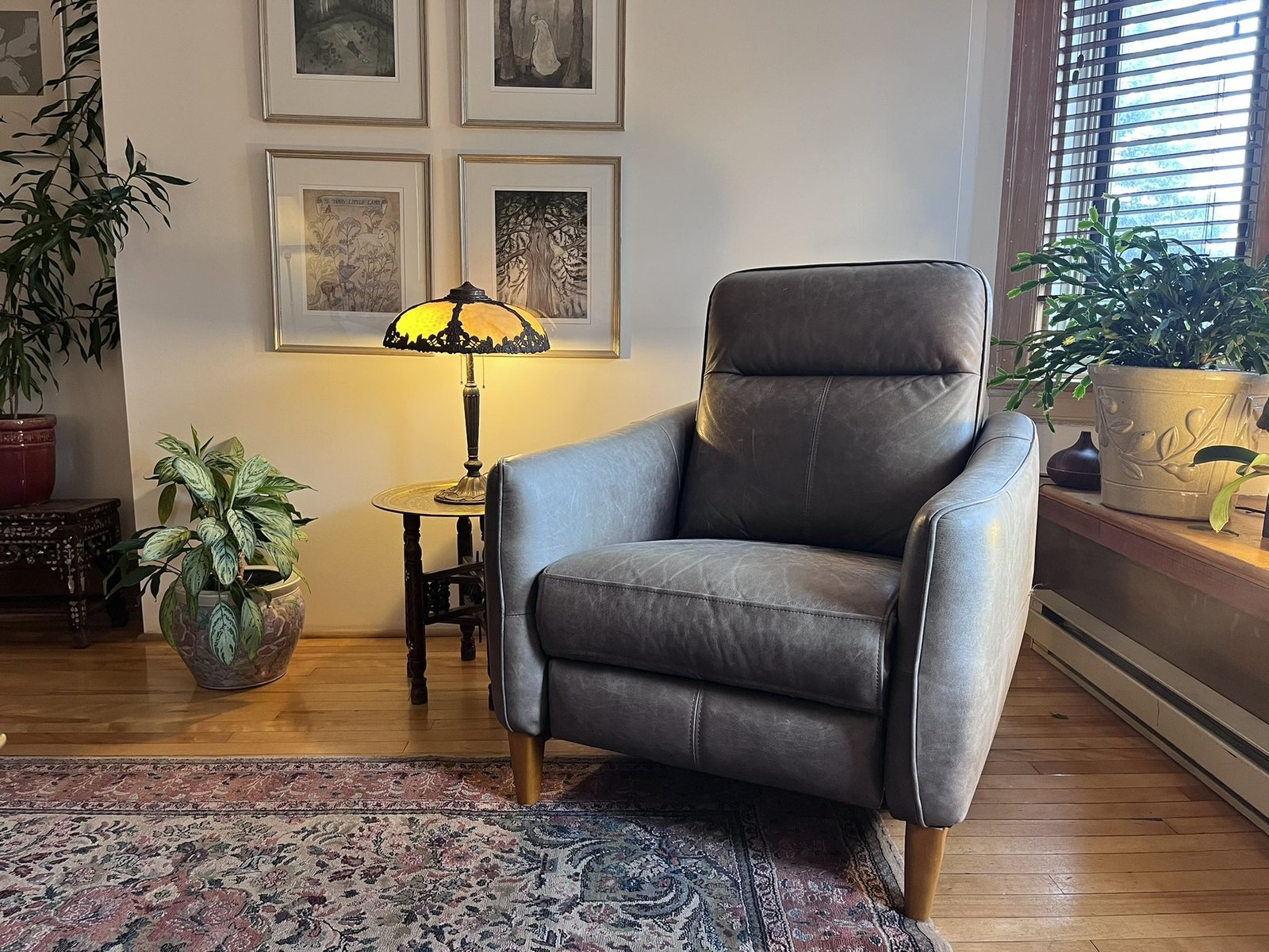 A grey leather recliner beside a glowing stained-glass lamp, framed prints and leafy plants in Mandy’s hypnotherapy office