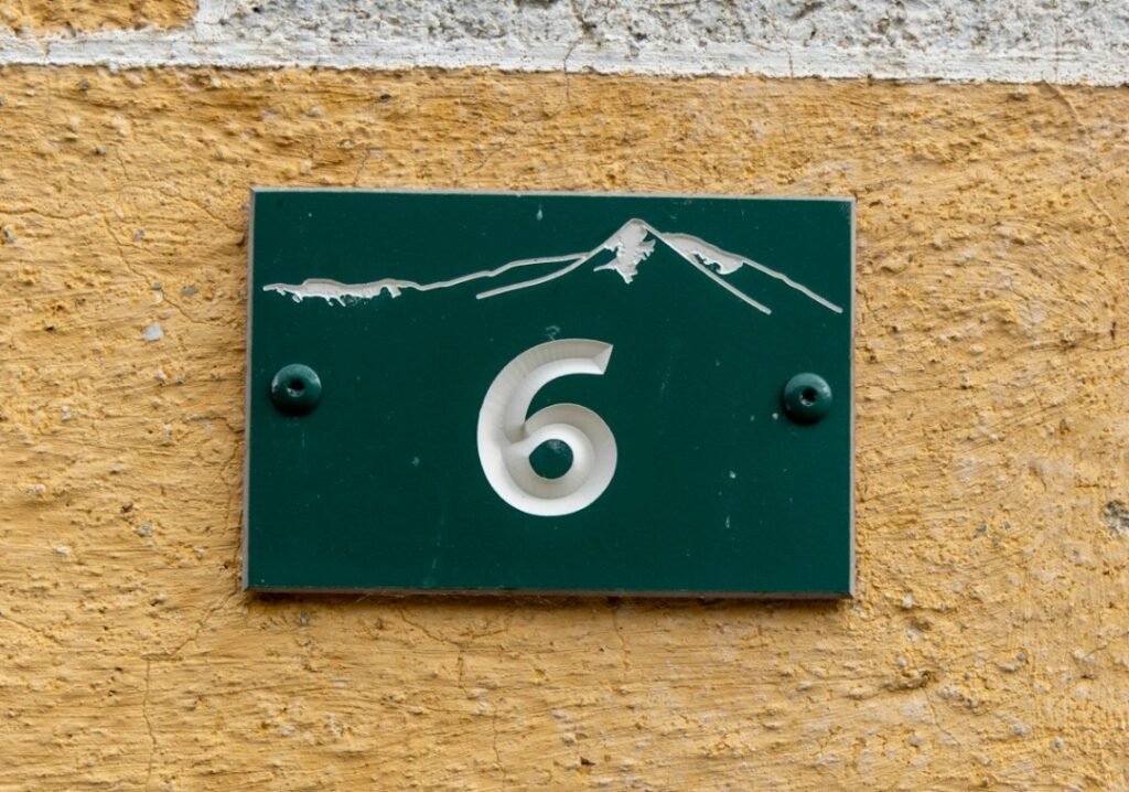 A green number 6 house plaque on a golden stone wall